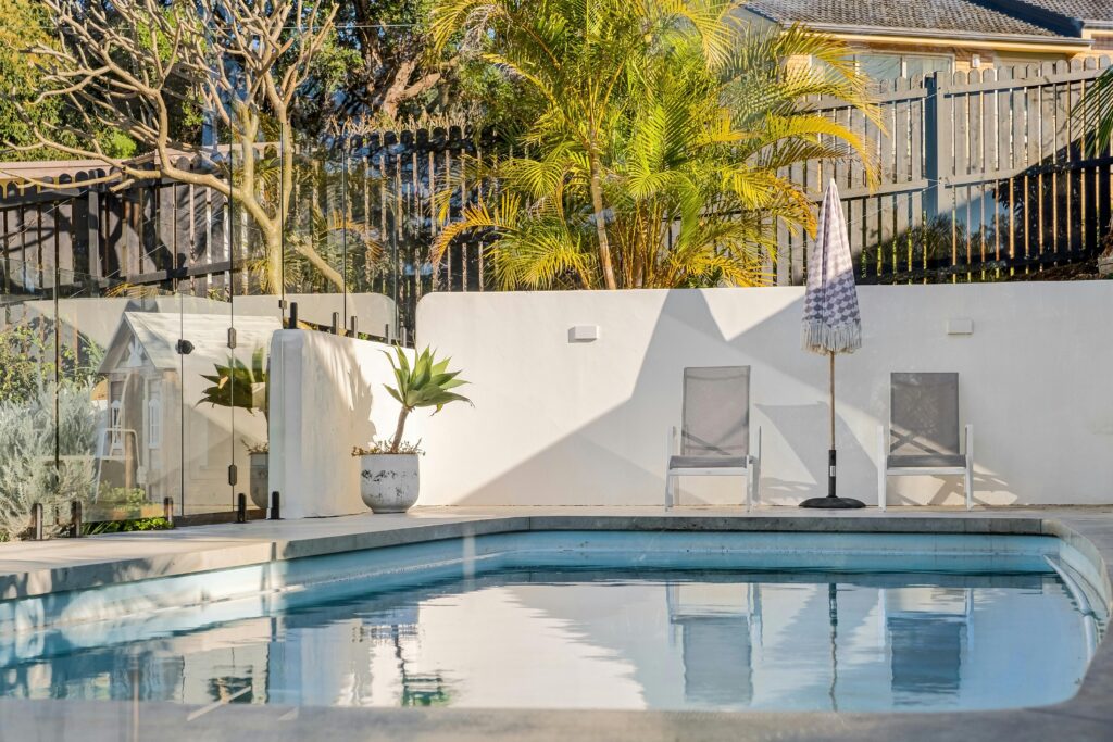 Modern backyard pool with glass fence and lounge chairs