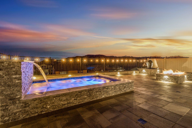 Evening spa with waterfall and fire pit by California Custom Pools