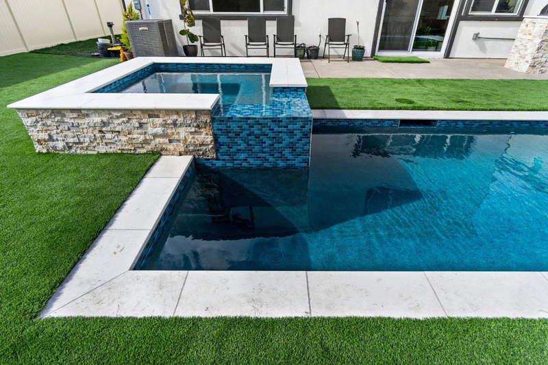 Raised spa beside modern backyard pool with turf