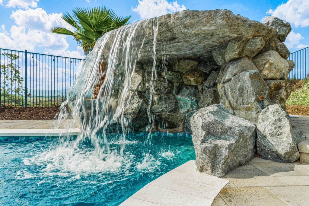 Rock waterfall pouring into a bright blue swimming pool