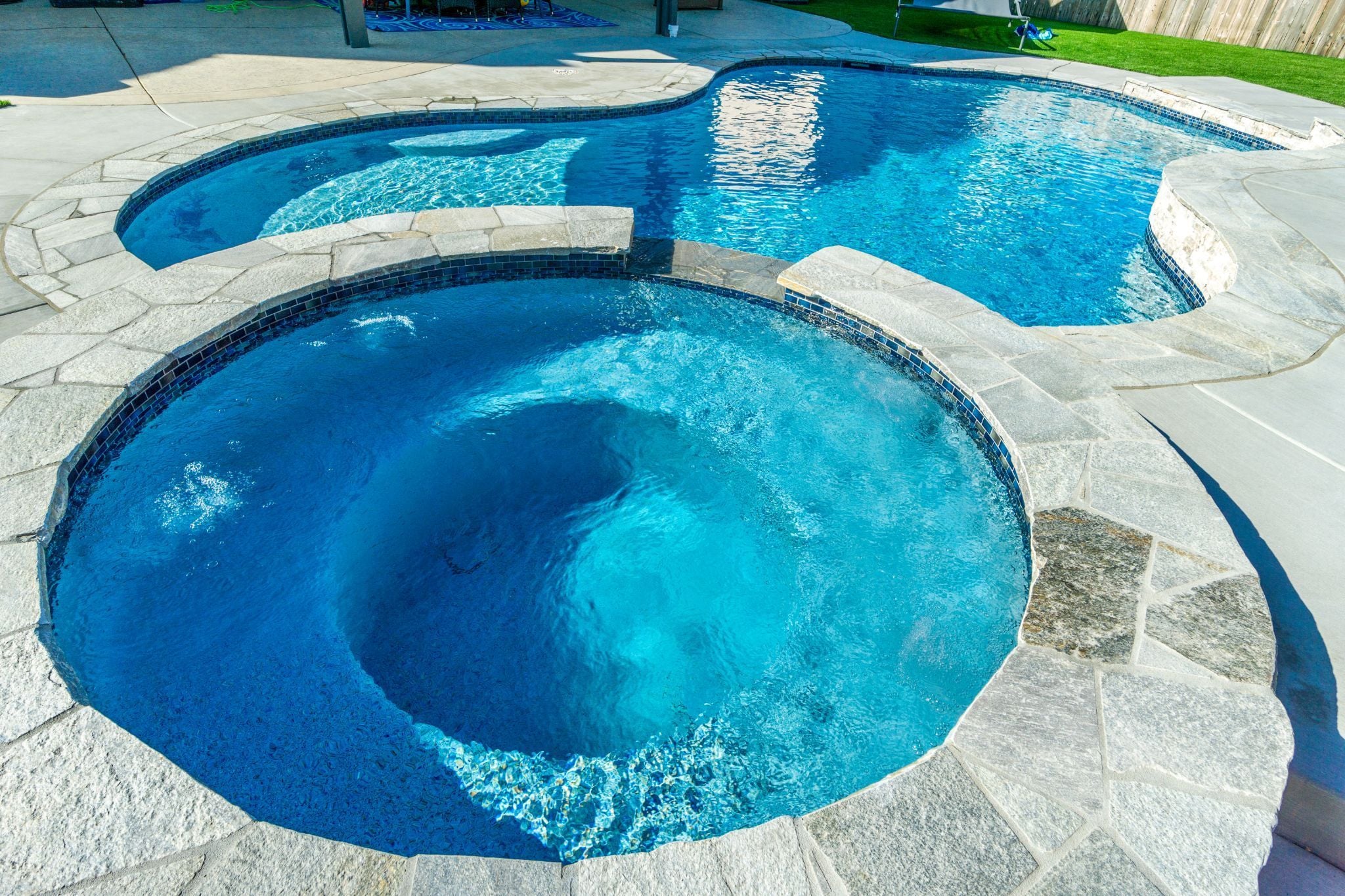 Freeform swimming pool with raised spa and stone coping