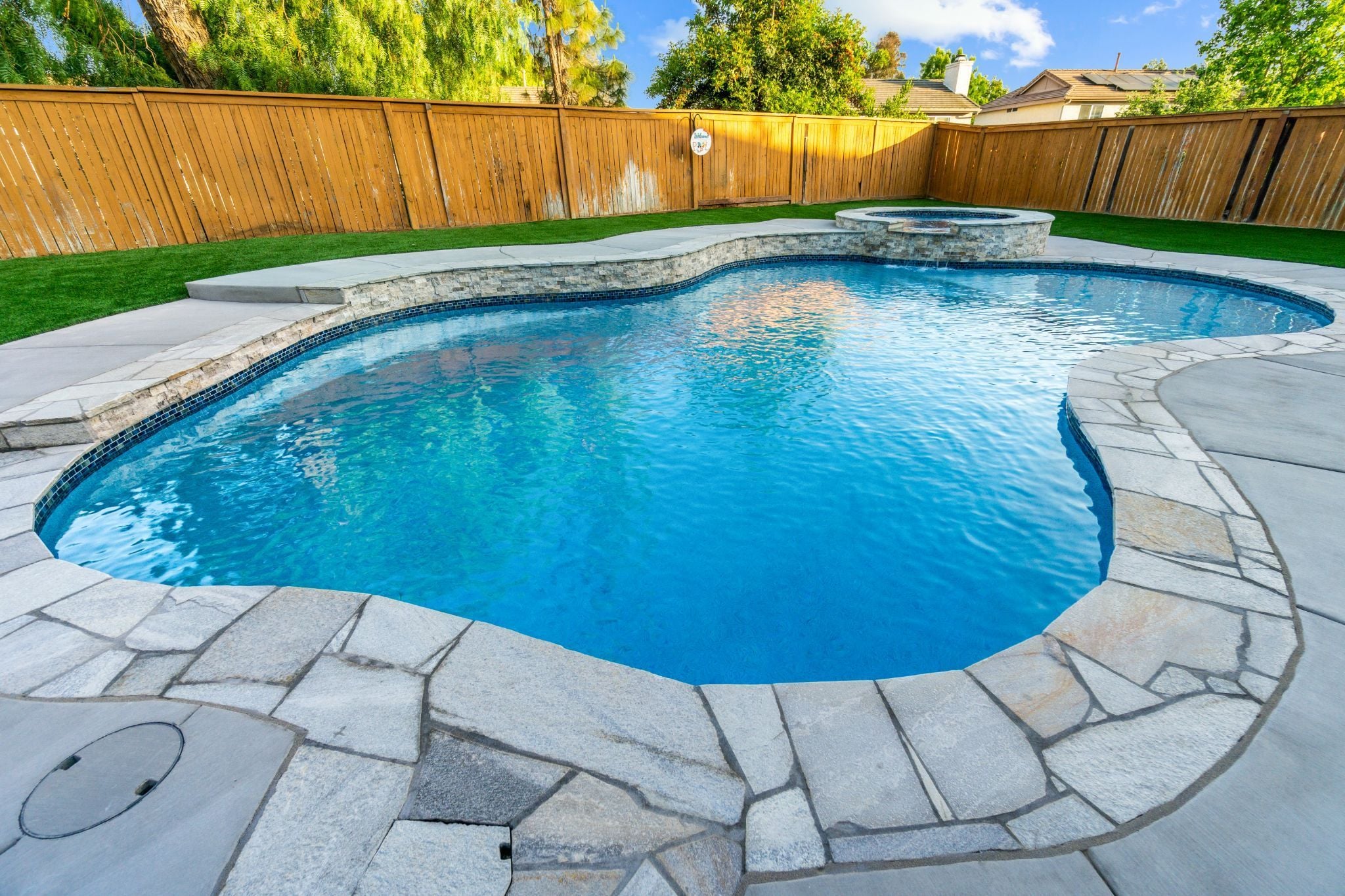 Freeform backyard pool with stone coping and raised spa
