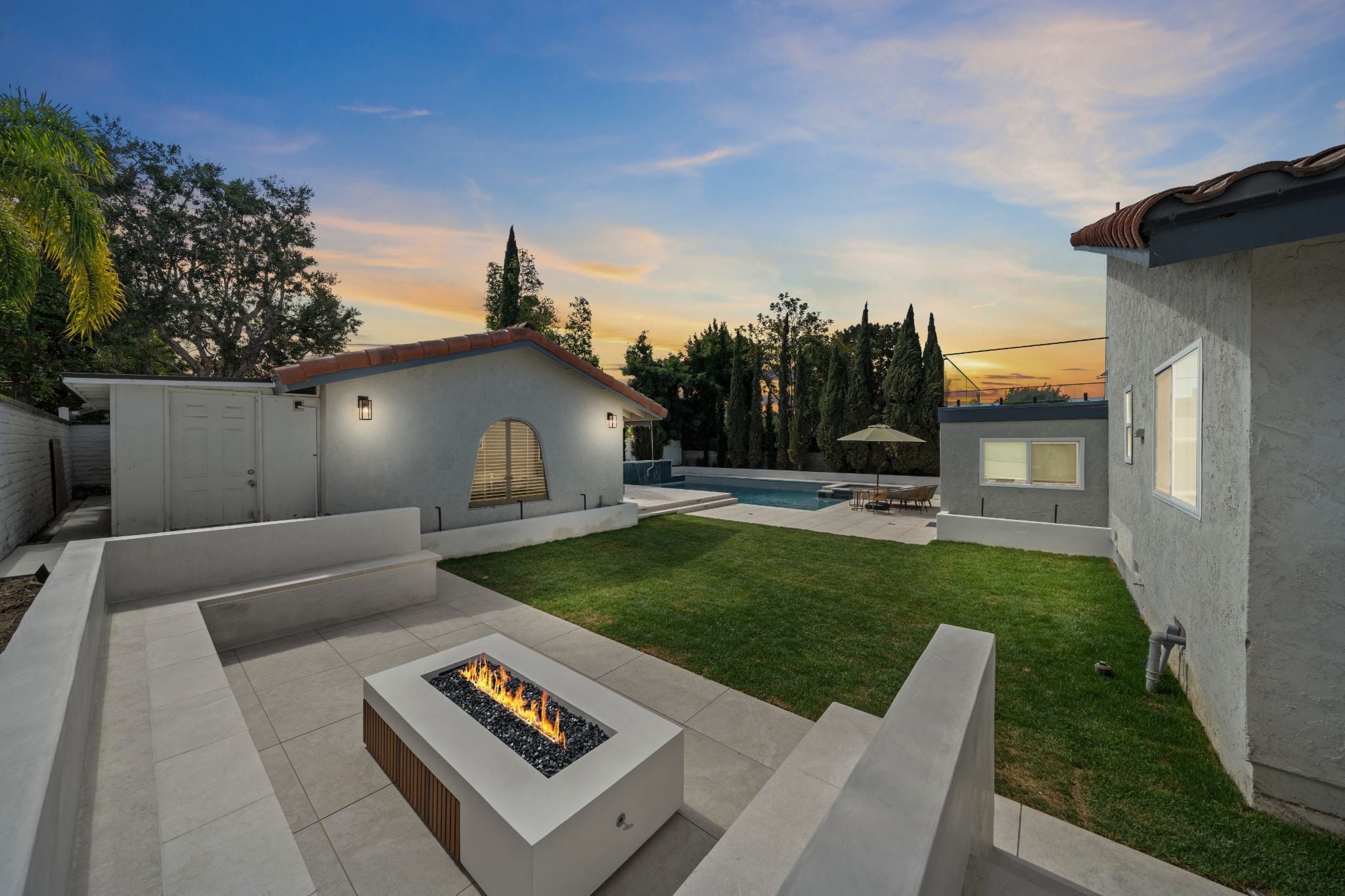 Backyard patio with fire pit, lawn, and pool at sunset